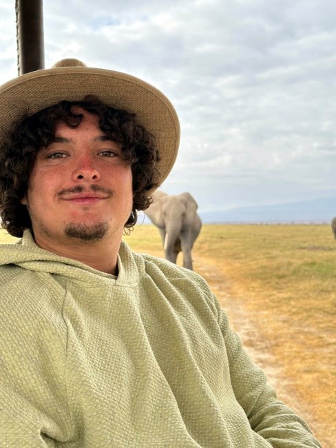Photo of Ben Ledet smiling in from of an elephant while wearing a hat.