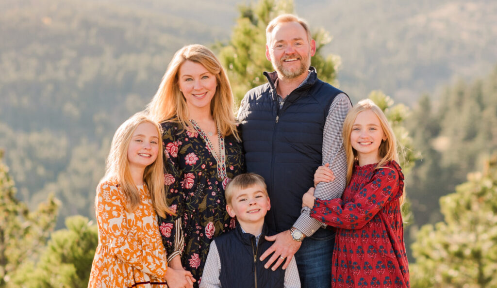 Tate family smiles and stands together while standing in front of mountains.