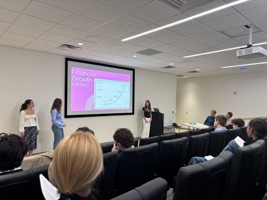 Three SAS students present to a crowd. The screen behind them reads "Financial Growth (EBITDA)."