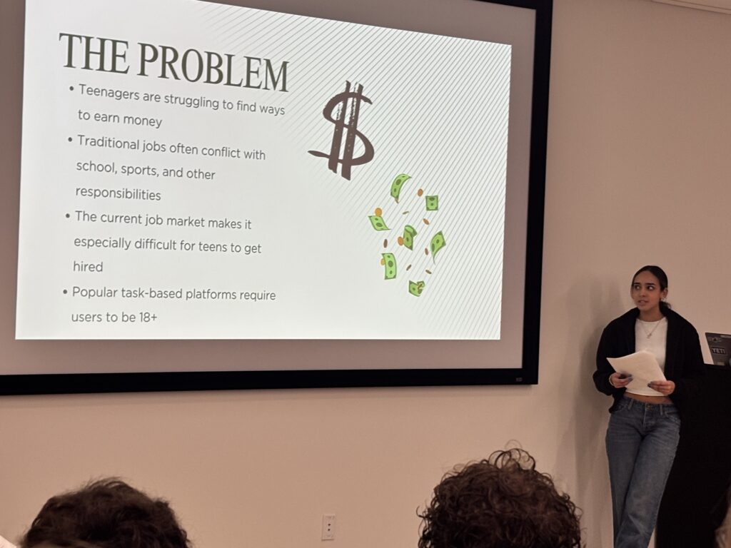 One SAS student holds a paper while speaking to. crowd. The screen beside her reads, "The Problem."