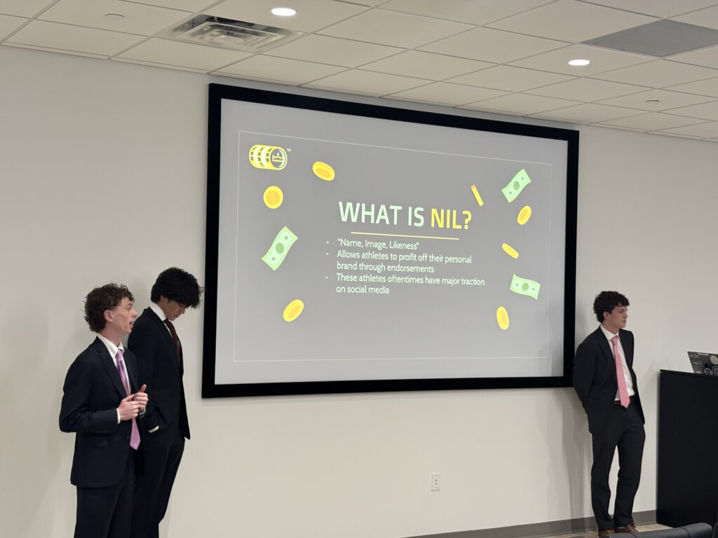 Three SAS students stand besides a screen and present. The screen reads, "What is NIL?"