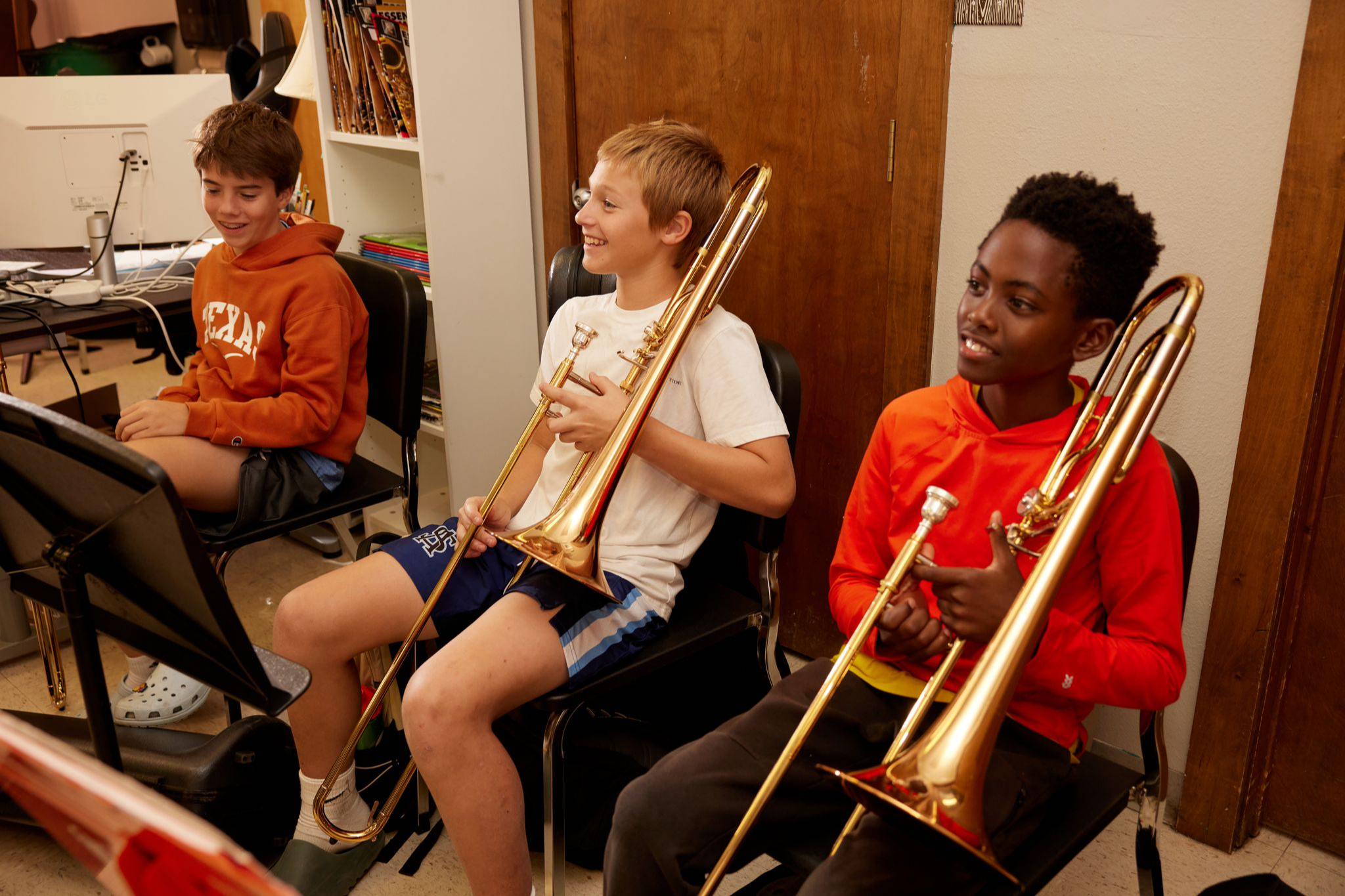 SAS Middle Schoolers smile in music class while holding trumpets.