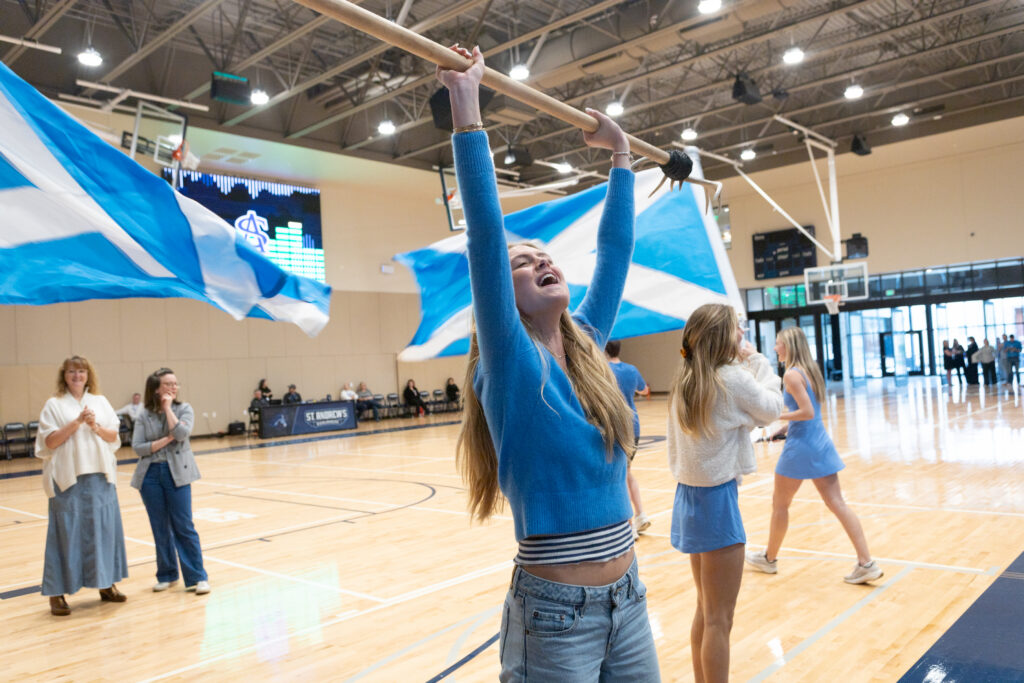 SAS student holds Scotland flag above her head with both arms while cheering.