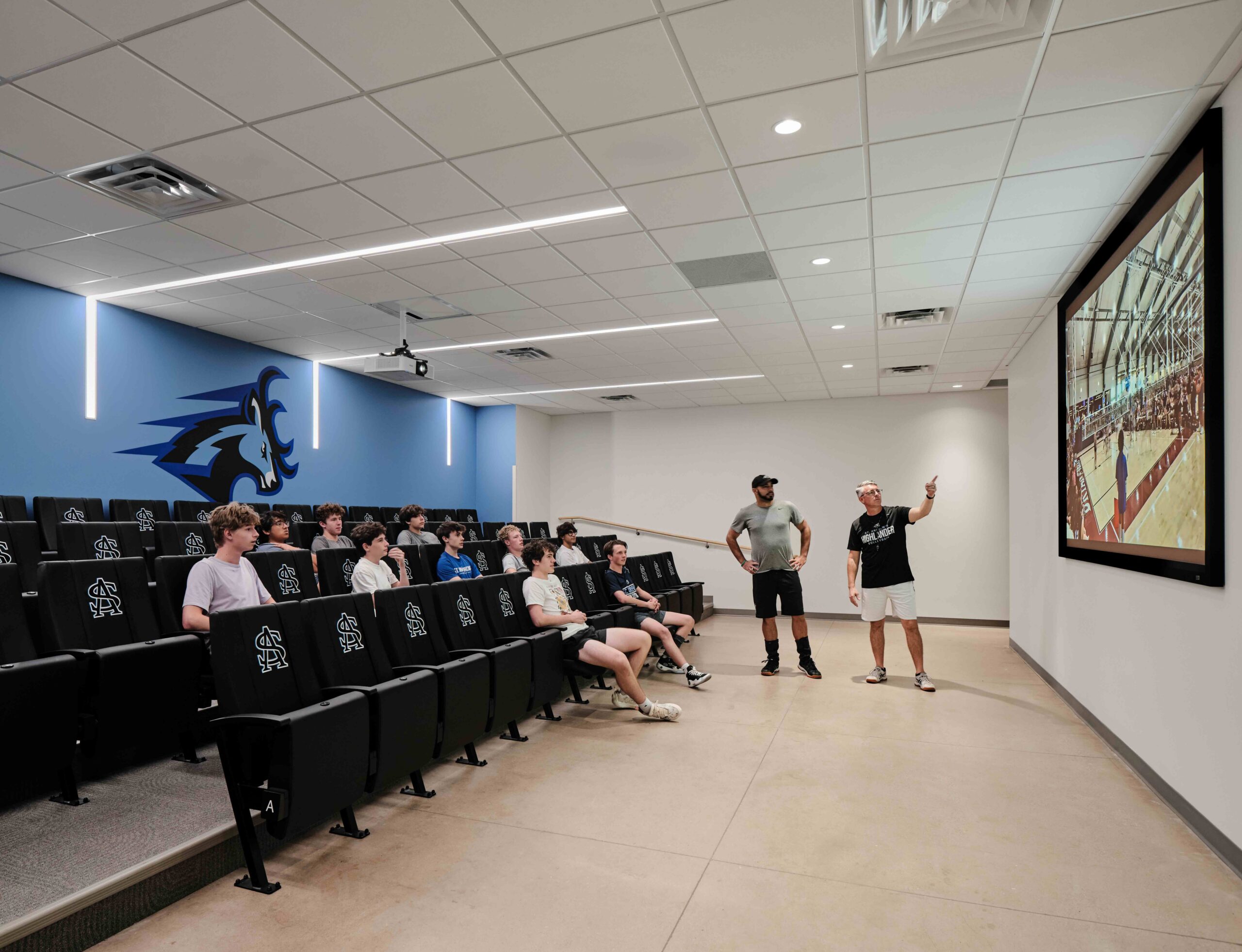 Students sit in chairs to watch their coach point at a screen in the film room.