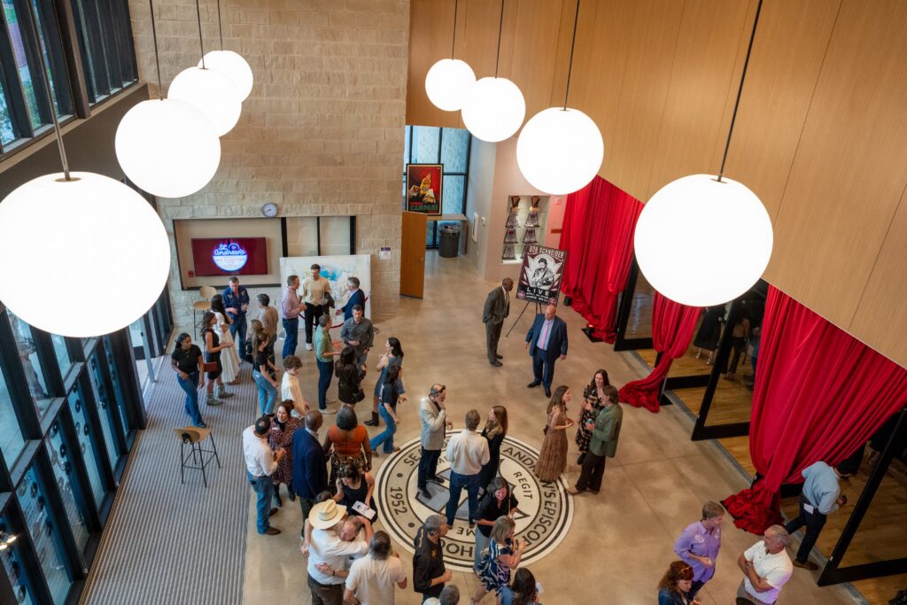 People gather in the Highlander Hall lobby and stand under bright circle lights hanging from the ceiling.