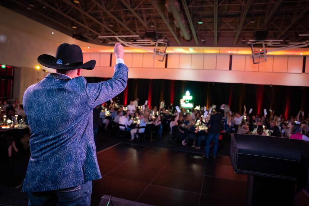 An auctioneer speaks to a crowd while standing on a stage.