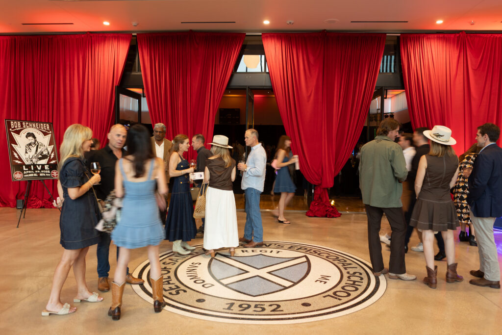 People stand outside the basketball court that was transformed into a music venue. There are red curtains that line the doors.