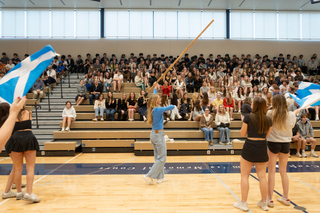 Students cheer in bleachers while students stand and wave flags.